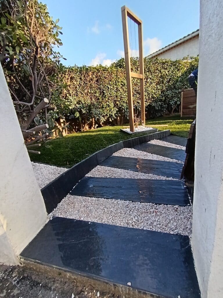 Allée de jardin en dalles noires et gravier blanc.