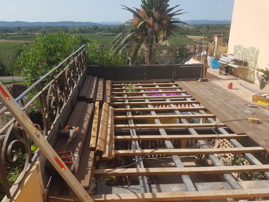 Chantier terrasse bois : lambourdes sur structure métal, planches et outils. Panorama avec palmier et vignes.