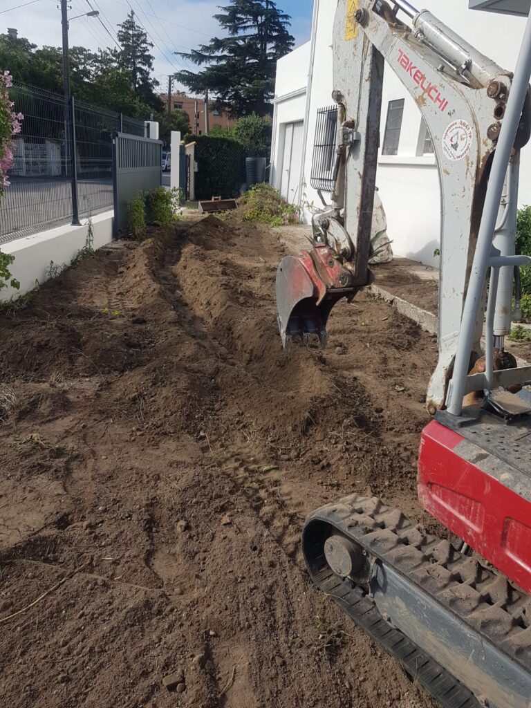 Mini-pelle Takeuchi creusant une tranchée dans un jardin en chantier.