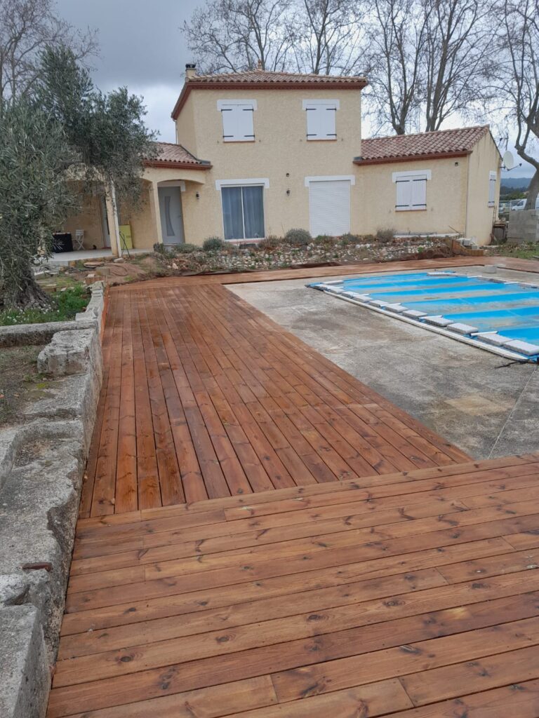 Terrasse en bois neuve entourant une piscine devant une maison provençale sous un ciel nuageux.